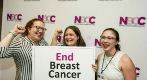 Three smiling NBCC staff members holding a sign that reads End Breast Cancer at the 2023 Advocate Leadership Summit
