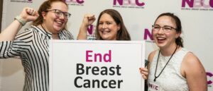 Three smiling NBCC staff members holding a sign that reads End Breast Cancer at the 2023 Advocate Leadership Summit