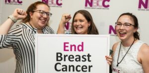 Three smiling NBCC staff members holding a sign that reads End Breast Cancer at the 2023 Advocate Leadership Summit
