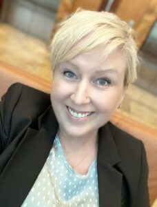 Brittany Lee, a smiling woman with short blond hair in a black jacket and a green and white top