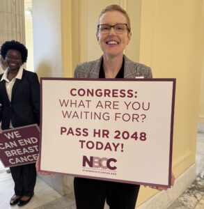 A woman with short hair and glasses holds a sign that reads Congress what are you waiting for pass HR 2048 today